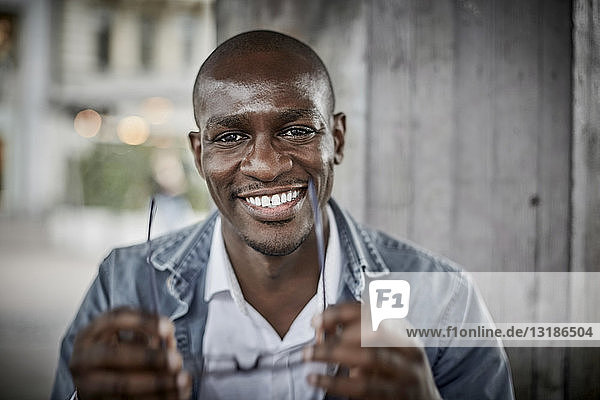 Portrait of smiling mid adult businessman holding eyeglasses in city