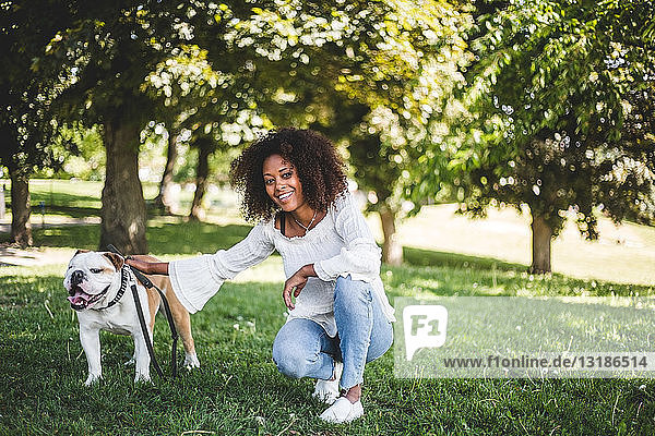 Portrait of smiling woman with bulldog on grassy field at park