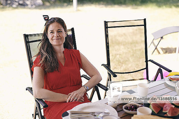 Nachdenklich lächelnde Frau  die auf einem Klappstuhl auf dem Campingplatz am Tisch sitzt
