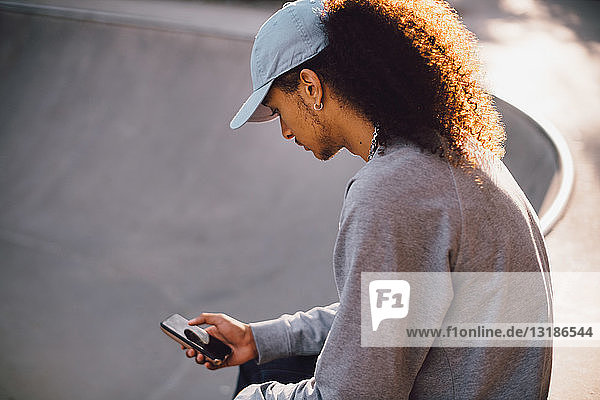 Junger Mann verschickt Textnachrichten auf Smartphone im Skateboard-Park