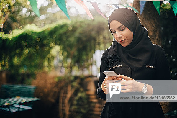 Junge Frau im Hidschab benutzt Smartphone während Gartenparty