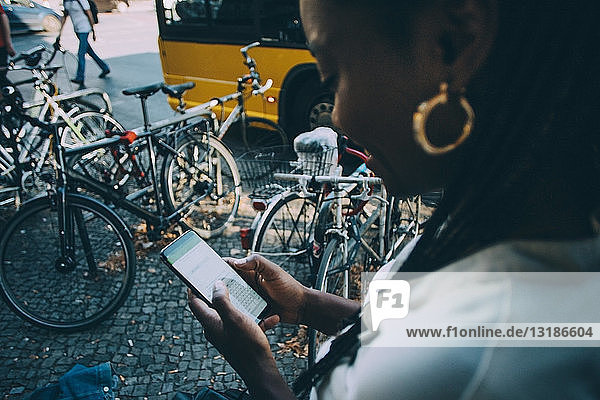 Junge Frau  die in der Stadt auf dem Bürgersteig stehend Textnachrichten über ein Smartphone verschickt