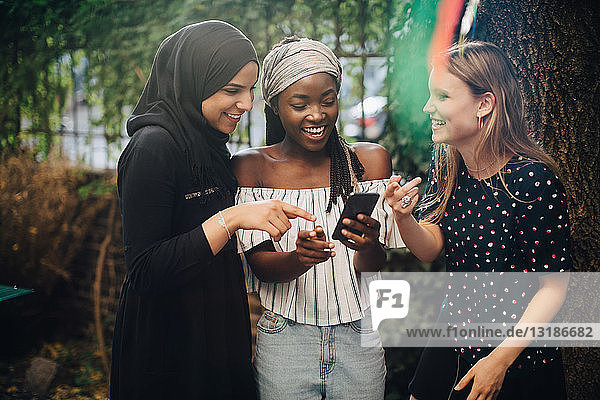 Lächelnde multiethnische Freundinnen  die im Hinterhof stehen und auf ihr Handy schauen
