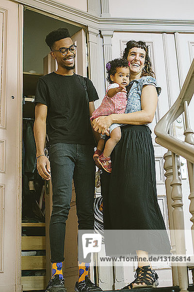 Happy mother and father with daughter at entrance in apartment