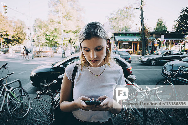 Junge Frau benutzt Mobiltelefon  während sie in der Stadt auf dem Bürgersteig steht
