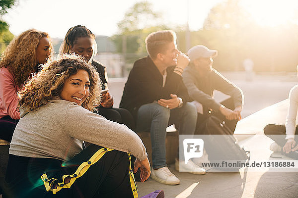 Portrait of smiling young woman sitting with friends at skateboard park