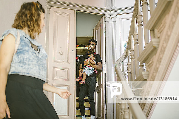 Junger Mann sieht Frau an  während er seine Tochter an der Tür trägt