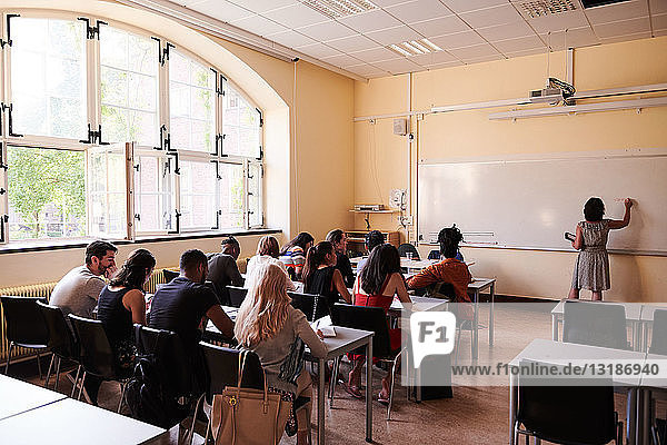 Lehrer schreibt am Whiteboard  während die Schüler im Klassenzimmer sitzen