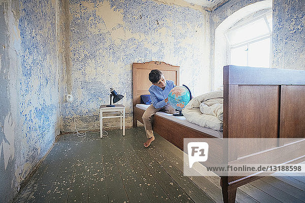 Junge schaut auf Globus auf rustikalem Bauernbett