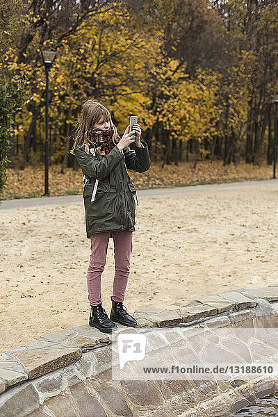 Tween girl using camera phone in autumn park
