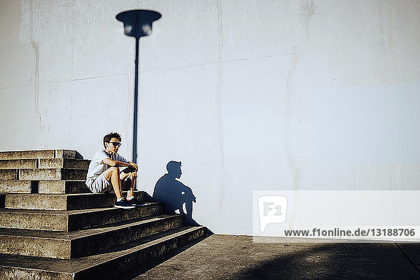 Junger männlicher Läufer  der sich auf einer sonnigen städtischen Treppe ausruht