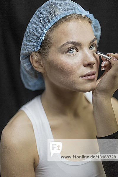 Visagistin trägt Make-up auf die Augen einer jungen Frau mit Duschhaube auf