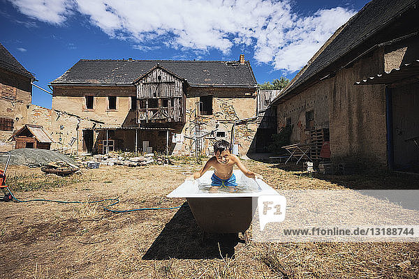 Verspielter Junge in der Badewanne auf einem sonnigen Bauernhof