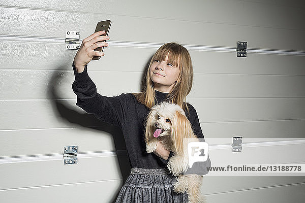 Mädchen mit Hund macht Selfie mit Fotohandy in Garage