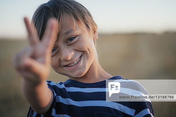 Porträt lächelnder  unbekümmerter Junge  der das Friedenszeichen macht
