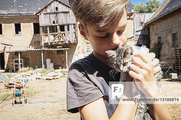 Affectionate boy kissing kitten on sunny farm