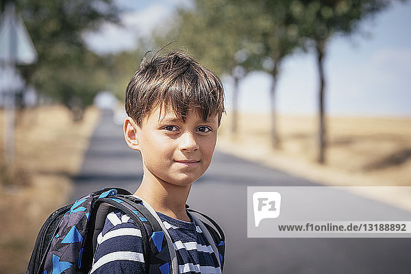 Portrait confident schoolboy with backpack on sunny road
