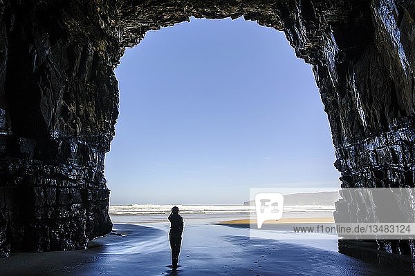 Frau steht im riesigen Eingang der Cathedral Caves im Gegenlicht  The Catlins  Südinsel  Neuseeland  Ozeanien