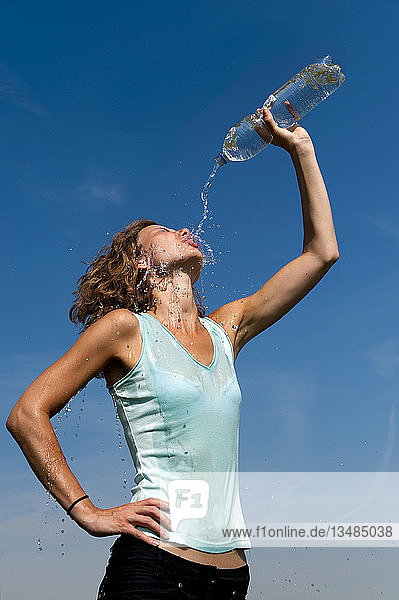 Junge Frau kippt sich den Inhalt einer Wasserflasche in das Gesicht