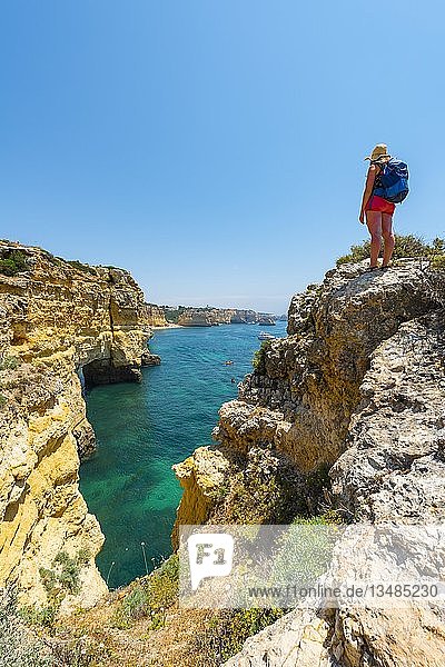 Junge Frau steht auf Felsen an Steilküste  Blick über türkisfarbenes Meer  Strand Praia da Marinha  zerklüftete Felsküste aus Sandstein  Felsformationen im Meer  Algarve  Lagos  Portugal  Europa