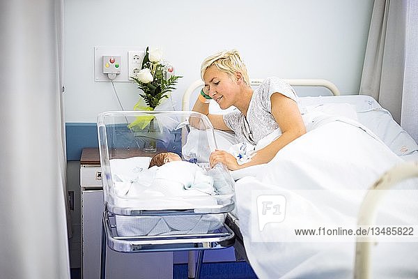 Eine Mutter betrachtet liebevoll ihr neugeborenes Kind  das noch im Krankenhaus liegt