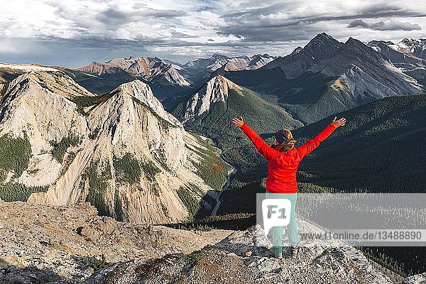 Wanderin mit erhobenen Armen schaut vom Gipfel über die Berglandschaft  Gipfel mit orangefarbenen Schwefelablagerungen  Panoramablick  Sulphur Skyline Trail  Nikassin Range  Jasper National Park  British Columbia  Kanada  Nordamerika