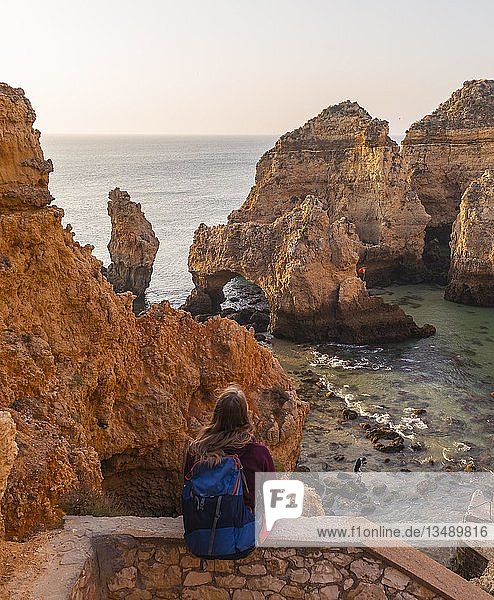Wanderin sitzt auf Steinmauer und schaut über Felsen ins Meer  Algarve Felsenküste  Ponta da Piedade  Lagos  Portugal  Europa