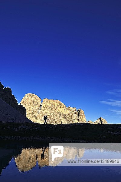 Wanderer am See im Gegenlicht  unterhalb des Paternalsattels  Drei Zinnen von Lavaredo  mit Blick auf den Zwölferkofel  Hochpustertal  Sextner Dolomiten  Südtirol  Italien  Europa