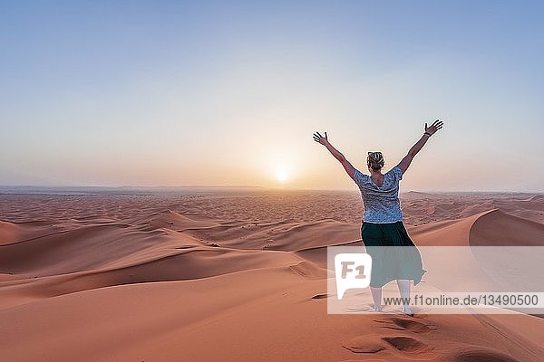 Wanderin streckt Arme in die Luft  rote Sanddüne in der Wüste  Sonnenuntergang  Erg Chebbi  Merzouga  Sahara  Marokko  Afrika