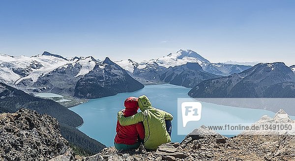 Blick vom Panorama Ridge Trail  Zwei Wanderer sitzen auf einem Felsen mit Garibaldi Lake  türkisfarbener Gletschersee  Guard Mountain und Deception Peak  Rückengletscher  Garibaldi Provincial Park  British Columbia  Kanada  Nordamerika