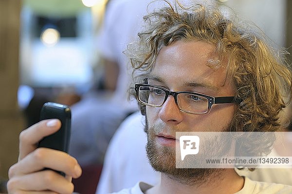 Junger Mann mit Brille schaut auf sein Handy