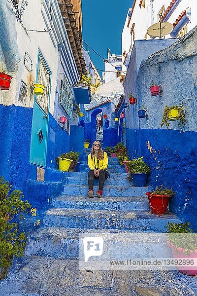 Junge Frau in der Altstadt sitzt auf einer Treppe Blaue Hauswände Medina von Chefchaouen Chaouen Tanger-Tétouan Marokko Afrika