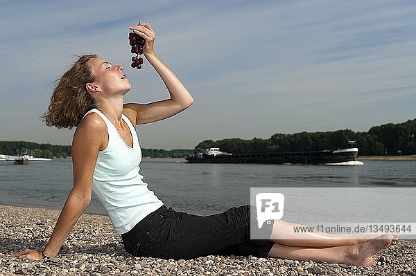 Junge Frau sitzt am Flussufer und isst Weintrauben