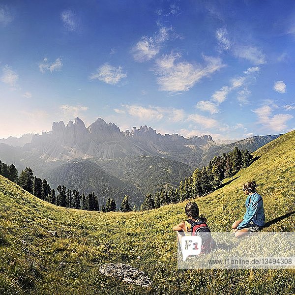 Hikers relaxing in a meadow enjoying the view of the Geisler group  Aferer Geisler mountains  Villnoesstal valley  province of Bolzano-Bozen  Italy  Europe