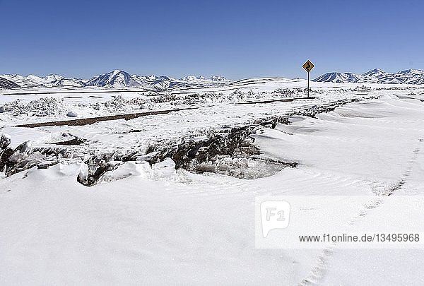 Tief verschneite Straße durch Atacama Wüste mit Verkehrsschild vor Anden Altiplano Bolivien Südamerika