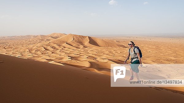 Wanderin läuft auf einer roten Sanddüne in der Wüste  Dünenlandschaft Erg Chebbi  Merzouga  Sahara  Marokko  Afrika