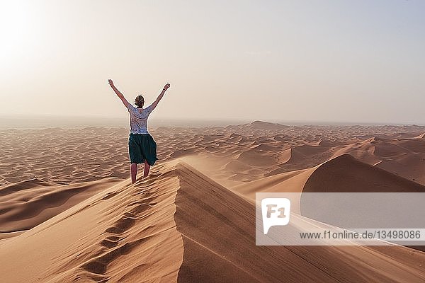 Wanderin hebt die Arme in die Luft  rote Sanddüne in der Wüste  Dünenlandschaft Erg Chebbi  Merzouga  Sahara  Marokko  Afrika