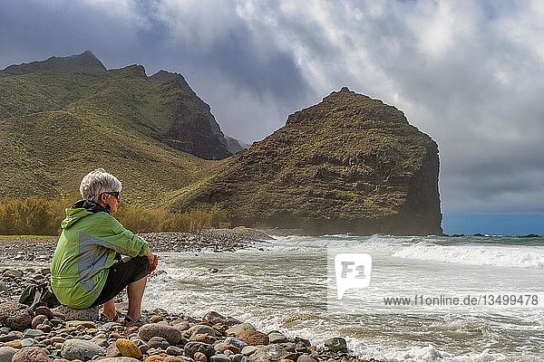 Tourist sits on the beach of Parque RubÃ©n Perez in front of Charco de la Aldea  Los Caserones  Gran Canaria  Spain  Europe