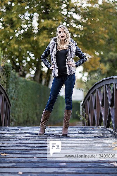 Young blonde woman poses confidently on a wooden bridge