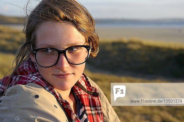 Eine junge Frau mit großer schwarzer Brille sitzt auf einer Düne  Bretagne  Frankreich  Europa