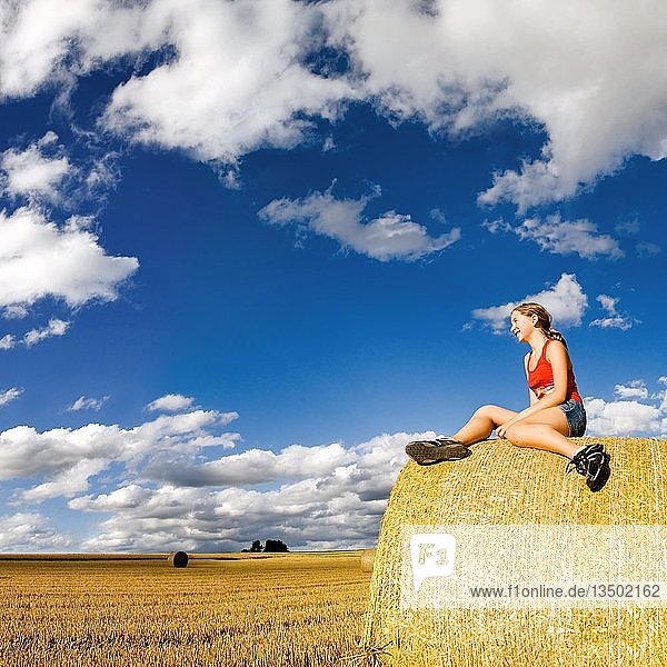 Abgeerntetes Getreidefeld  mit einer Frau  die auf einem runden Strohballen sitzt  unter ungewöhnlichen Wolkenformationen im Nachmittagslicht