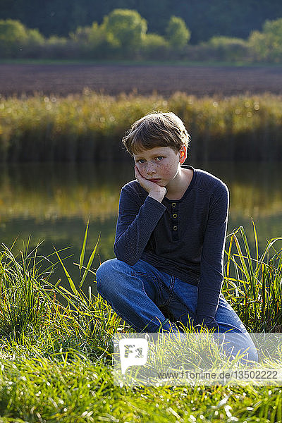 Sad boy sitting on a small lake  Wandersleben  Thuringia  Germany  Europe