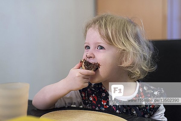 Kleines blondes Mädchen beißt in ein Brötchen mit Schokoocreme Deutschland Europa