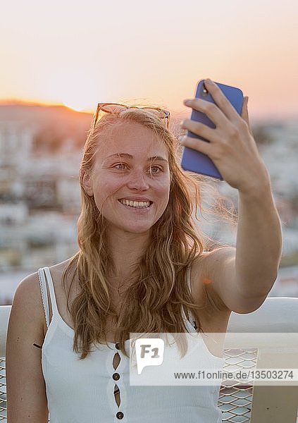 Junge Frau mit weißem Top fotografiert sich selbst mit einem Smartphone Portrait Selfie Sonnenuntergang Plaza de la Encarnacion Sevilla Andalusien Spanien Europa