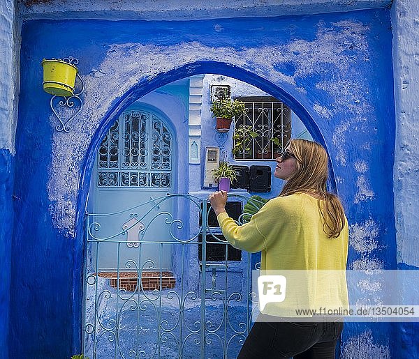Junge Frau vor einem Tor  blaue Hausfassade  Altstadt  Medina von Chefchaouen  Chaouen  Tanger-Tétouan  Marokko  Afrika