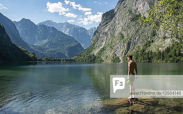 Junger Mann steht auf einem Stein im Obersee  hinter dem Watzmannmassiv  Salet am Königssee  Nationalpark Berchtesgaden  Berchtesgadener Land  Oberbayern  Bayern  Deutschland  Europa