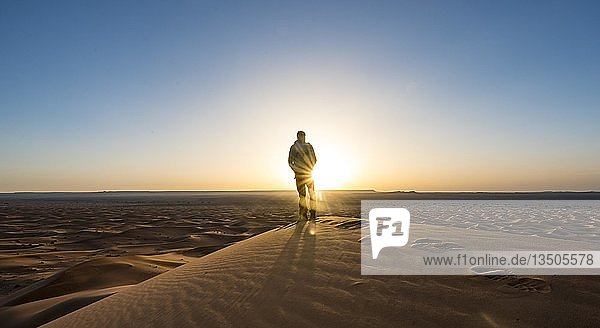 Junger Mann steht auf einer Sanddüne  Sonnenstrahlen bei Sonnenaufgang  Erg Chebbi  Merzouga  Sahara  Marokko  Afrika