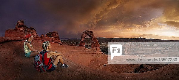 Hikers sit at Delicate Arch Arch  Dusk  Arches National Park  near Moab  Utah  USA  North America