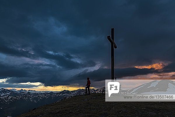 Gipfelkreuz Sattele mit Bergsteiger bei Sonnenaufgang  dramatische Wolken  Sarntaler Alpen  San Martino  Sarntal  Südtirol  Italien  Europa