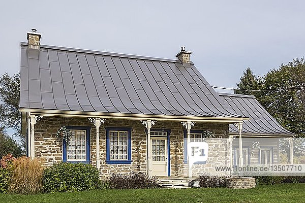 Alte Feldsteinfassade im Landhausstil von 1820 mit blauer Zierleiste und braunem Stehfalz-Blechdach sowie Anbau aus gestapelten Baumstämmen im Herbst  Quebec  Kanada  Nordamerika